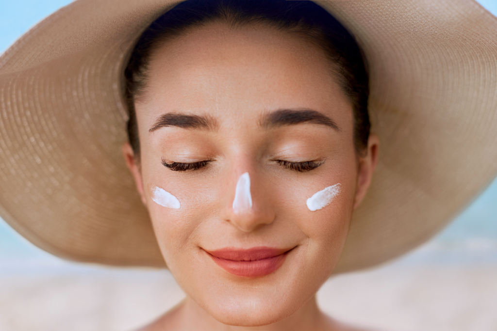 Happy young woman protecting face with hat and sunscreen