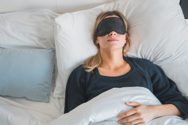 Woman sleeping on back with eye mask to protect her eyes and improve sleep quality